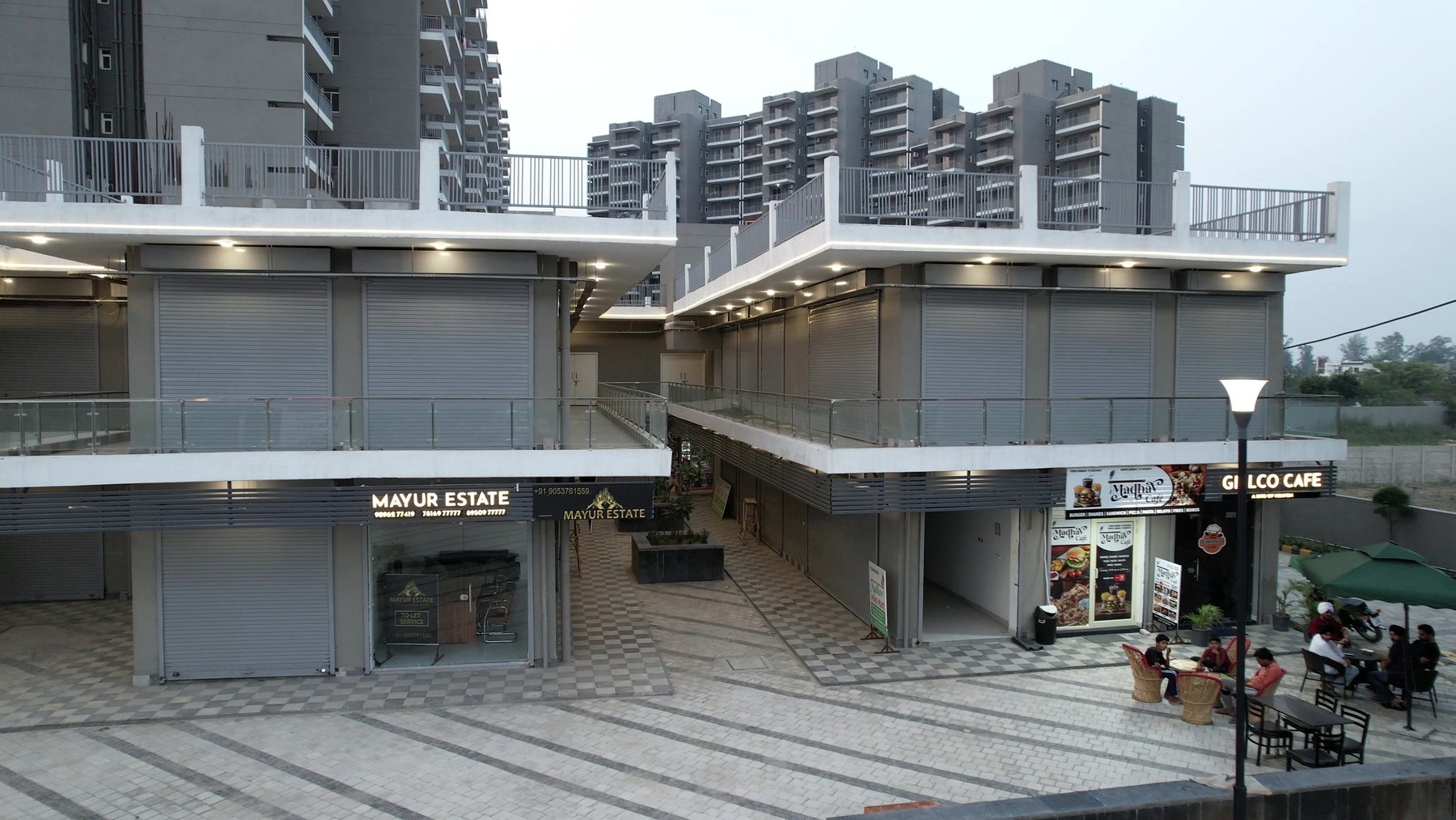 Ground- and upper-level shopfronts with café seating at Kalpana Chawla Space.